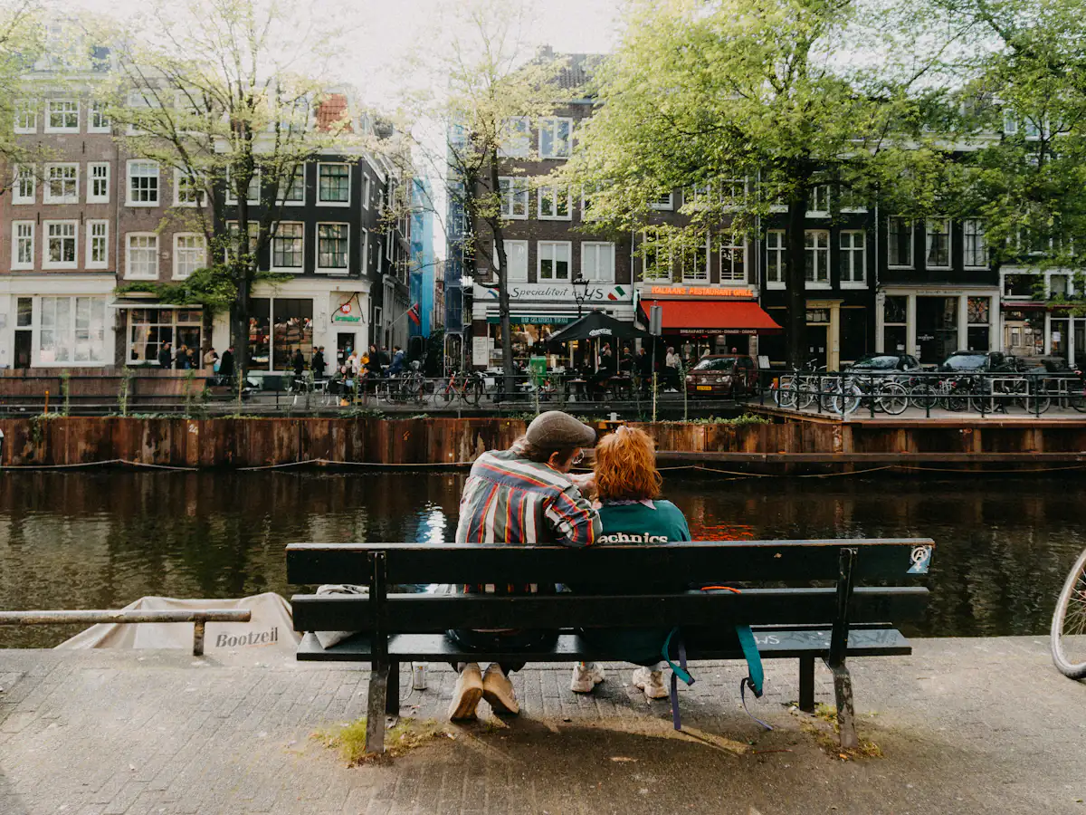 Two people sitting on a bench beside an Amsterdam canal