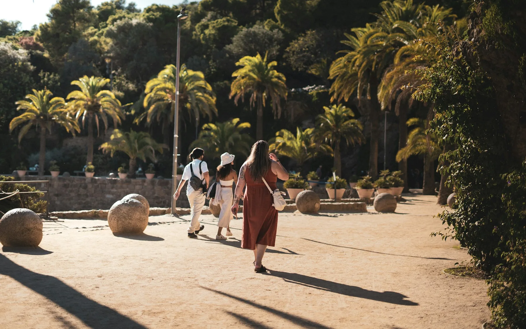Two people walking through a sunny Barcelona park with palm trees
