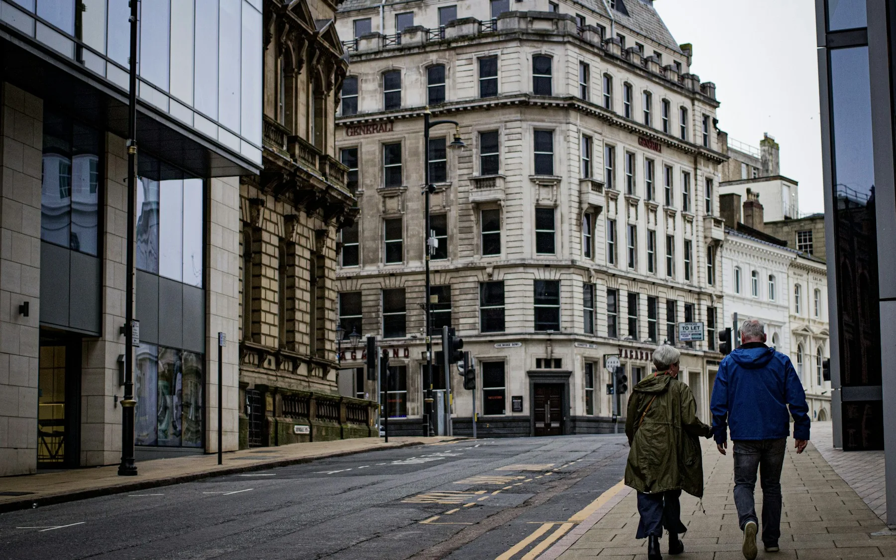 A man and a woman walking down a street between Birmingham city-centre buildings, photographed from behind