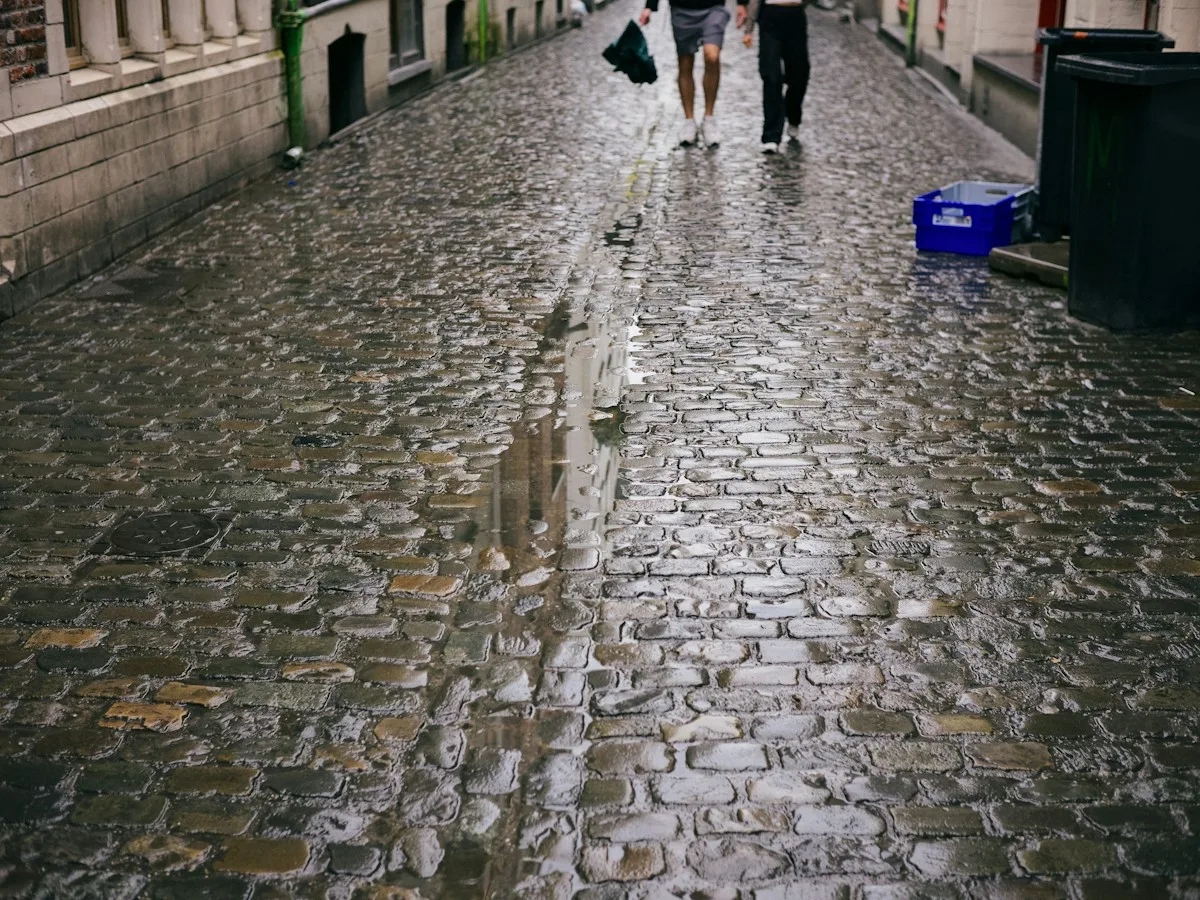 Two people walking down a wet cobbled street in Brussels