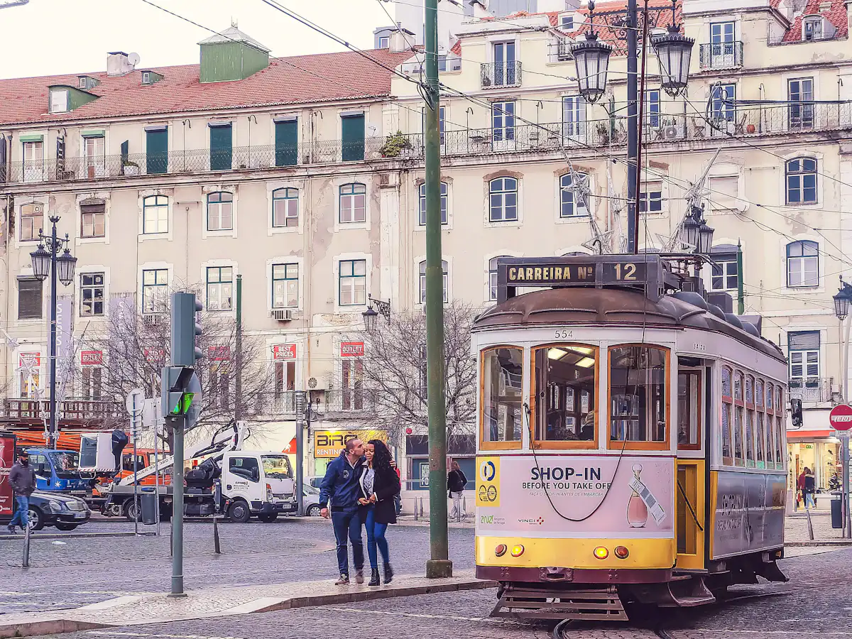 Two people standing beside a yellow tram in Lisbon