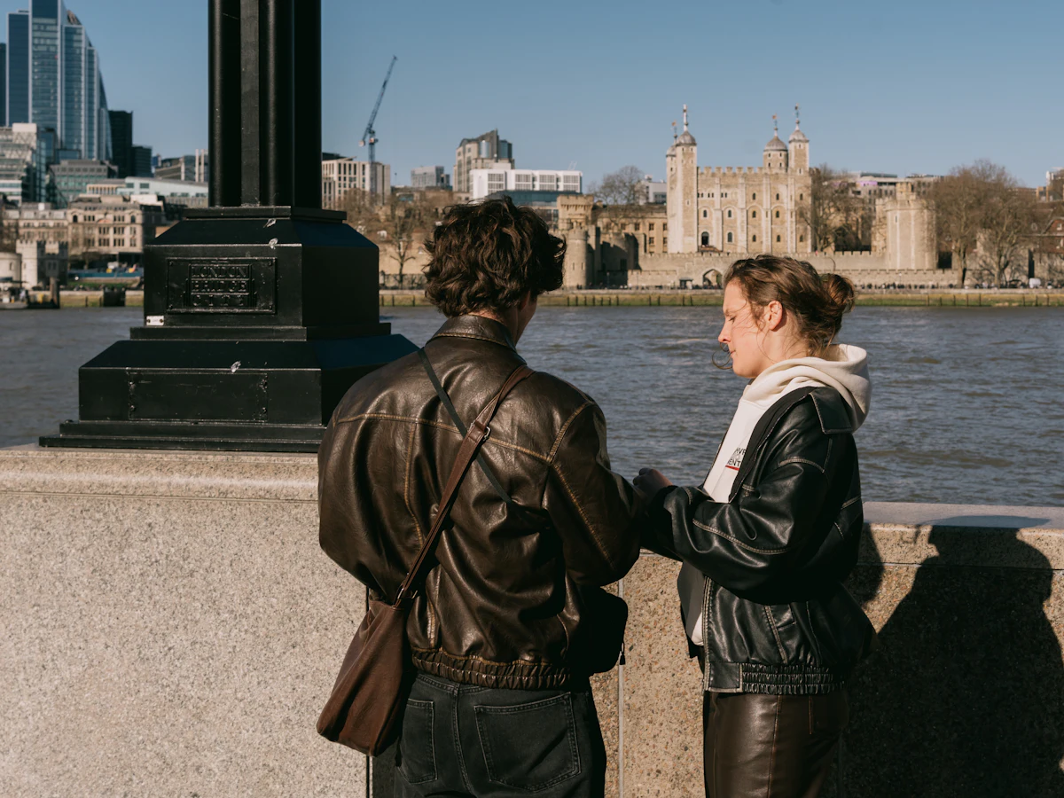Two people talking beside the river Thames with the Tower of London behind