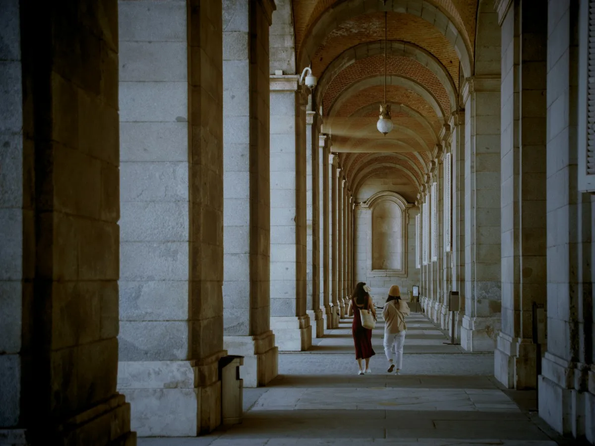 A couple walking away down a long stone arcade in Madrid