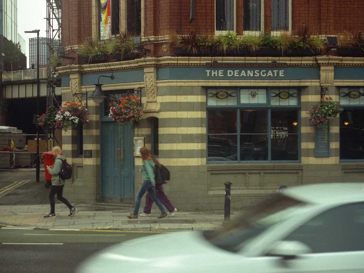 Two people walking past a pub on Deansgate in Manchester