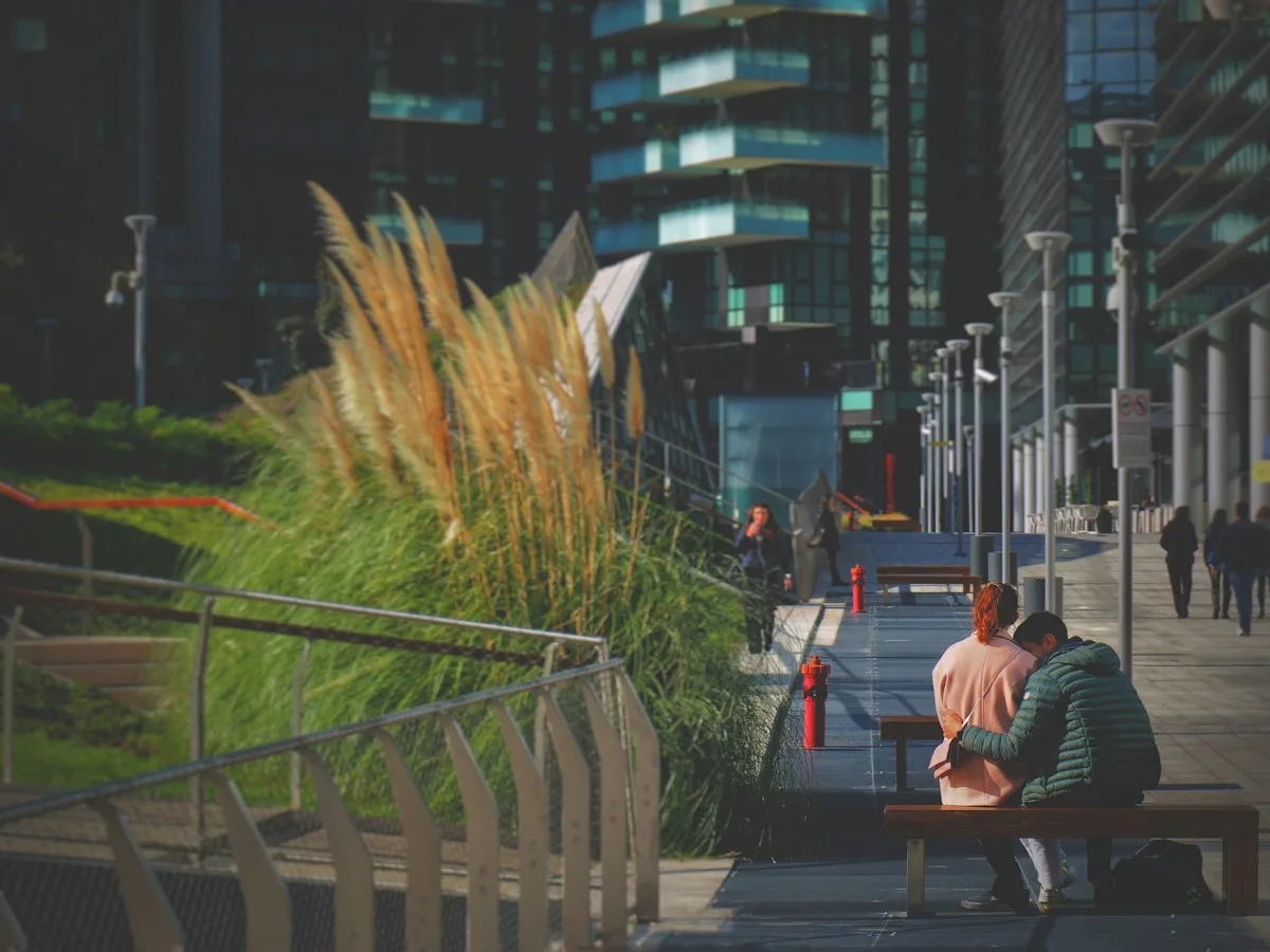 A man and a woman sitting on a bench beside tall grasses in Milan