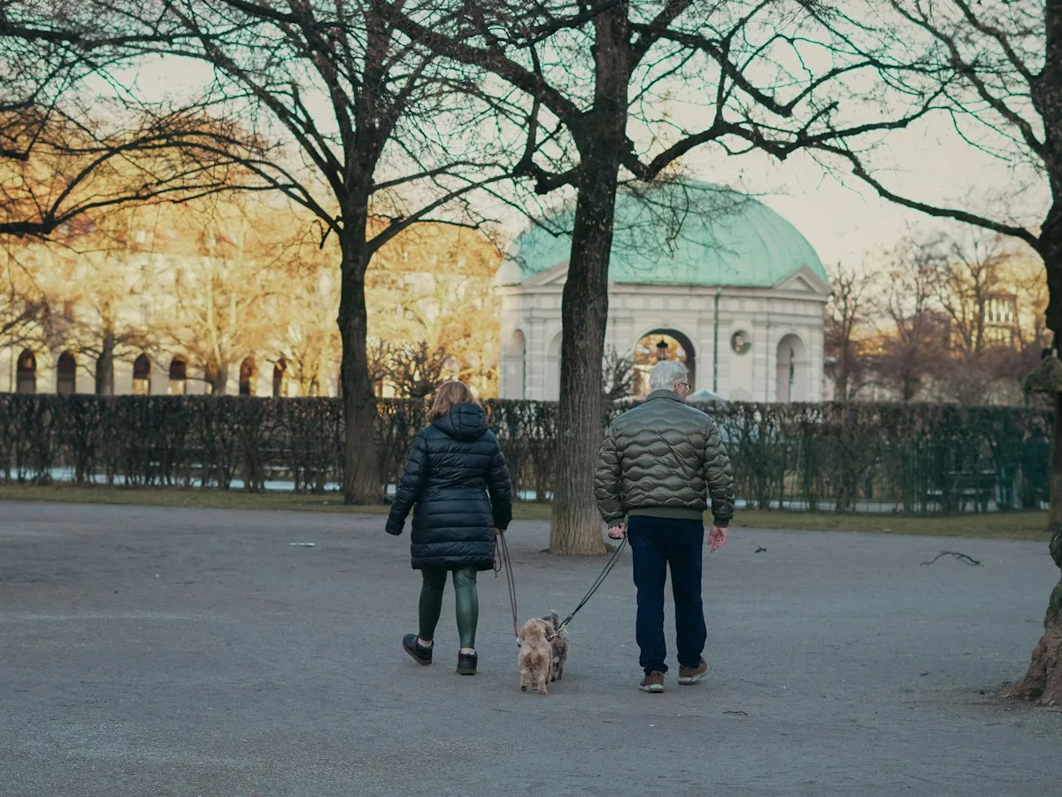A man and a woman walking a dog through the Hofgarten in Munich