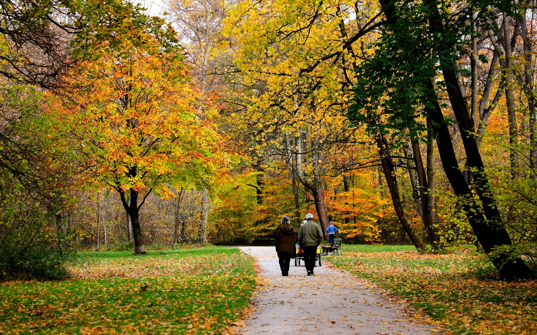Two people walking down a leaf-covered path in a Munich park in autumn