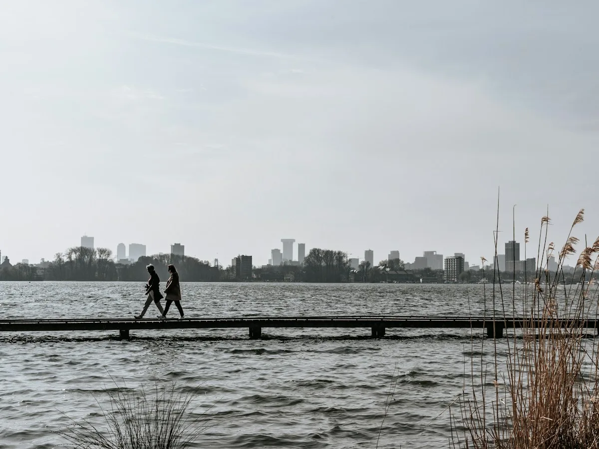 Two people walking along a jetty with the Rotterdam skyline in the distance
