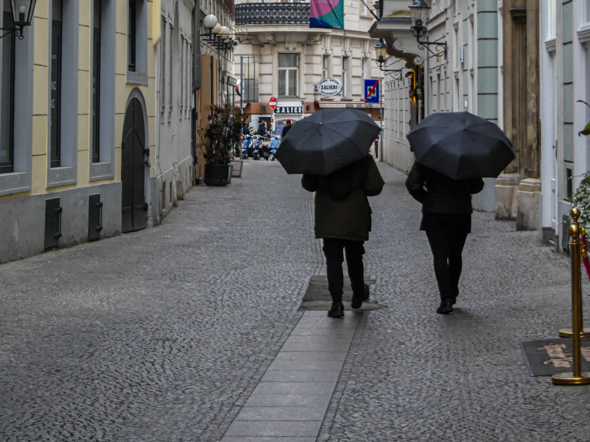 Two people with umbrellas walking down a cobbled street in central Vienna