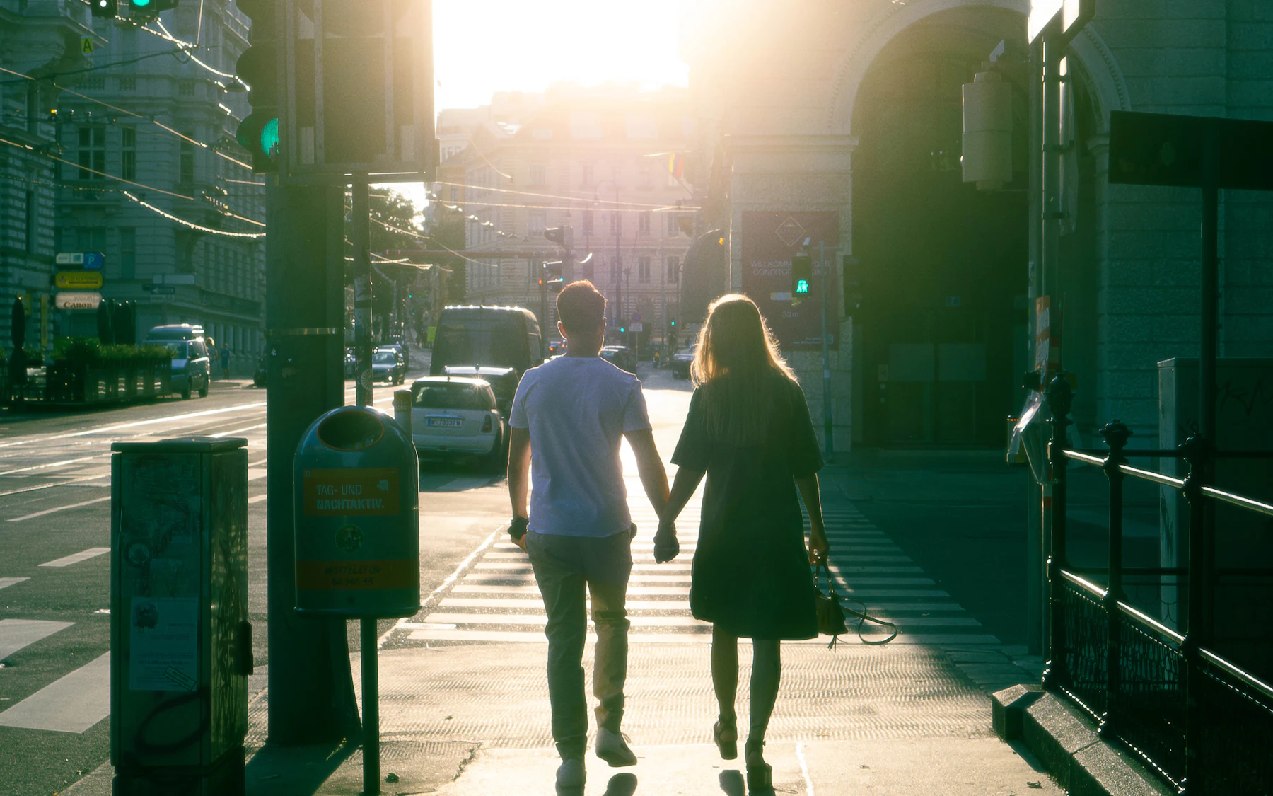 A couple holding hands and walking down a Vienna street towards the evening sun