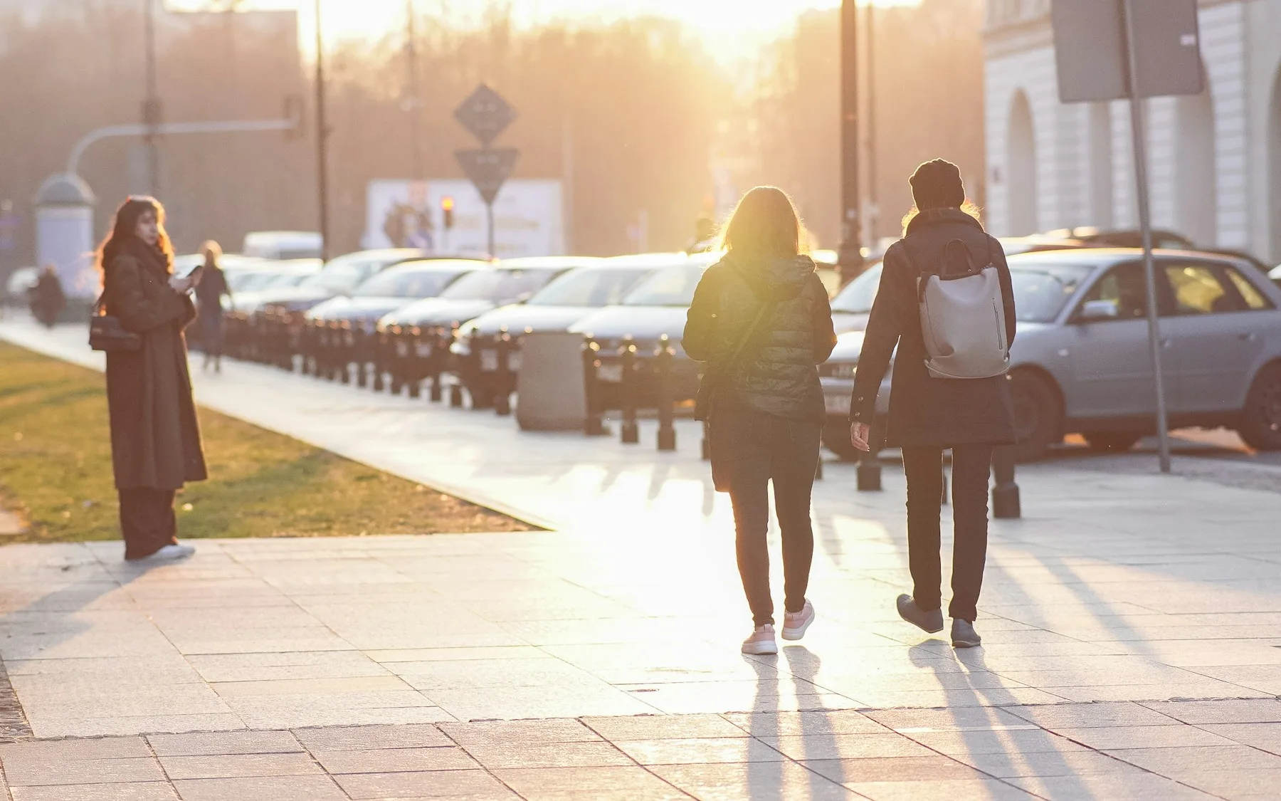 Two people walking down a Warsaw street in low evening sun, photographed from behind